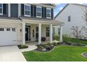 Inviting front porch with decorative columns, black door, rocking chairs, and landscaped garden at 5363 Citadel Dr, Noblesville, IN 46062