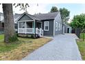 View of home with gray siding, covered porch, gravel driveway, and a detached garage at 1504 Manhattan Ave, Indianapolis, IN 46241