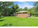 View of a single-story brick home with an attached garage and overgrown landscaping and grass on a sunny day at 10159 Hodge Rd, Clayton, IN 46118