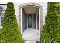 Inviting front porch with brick archway, evergreen shrubbery and black front door at 3720 Abney Highland Dr, Zionsville, IN 46077