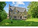 Two story stone home with chimney, arched doorway, bay window, and covered patio on a landscaped lawn at 2421 W 39Th St, Indianapolis, IN 46228