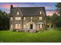 Night shot of stone home with peaked roof, multiple arched windows, covered porch, and manicured front lawn at 2421 W 39Th St, Indianapolis, IN 46228