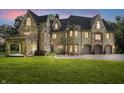Stone home with arched entry to covered patio, attached garage, and illuminated windows at dusk at 2421 W 39Th St, Indianapolis, IN 46228