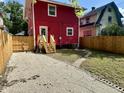 View of the fenced backyard, and side entry with stairs on the back of the red house at 2423 E 13Th St, Indianapolis, IN 46201