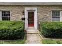 Close up of the facade of a stone home, highlighting the red front door and manicured shrubbery at 6030 Evanston Ave, Indianapolis, IN 46220