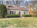 Cottage-style home with a stone facade, a red front door, manicured bushes, and mature trees at 6030 Evanston Ave, Indianapolis, IN 46220