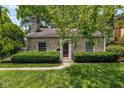 A charming stone home with a red front door, well-maintained landscaping, and mature trees at 6030 Evanston Ave, Indianapolis, IN 46220