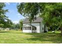 Exterior side view of a charming white house featuring a sunroom, set against a backdrop of lush greenery at 16000 W 700 S, Anderson, IN 46017