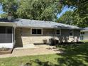 Exterior view of the home's rear with a patio and a well-maintained lawn surrounded by lush trees at 3906 N Lanewood Dr, Muncie, IN 47304