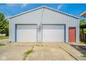 Large detached garage with two white doors, a red side door, and a concrete apron at 4644 E 150 N, Anderson, IN 46012
