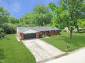 Aerial view of a brick house with an attached garage, green lawn and mature trees, surrounded by more greenery at 7234 Fairwood Dr, Indianapolis, IN 46256