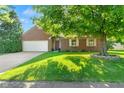 Charming brick home with an attached two-car garage, lush lawn, and a large mature tree at 7239 N Orchard Dr, Indianapolis, IN 46236