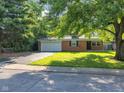Charming brick home featuring an attached garage, freshly cut lawn, and mature trees providing ample shade at 1231 N Graham Ave, Indianapolis, IN 46219