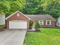 Quaint brick home featuring an attached garage, mature landscaping, and a well-maintained lawn at 5935 Oakforge Ln, Indianapolis, IN 46254