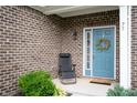 Home's welcoming blue front door and a cozy porch setting with a chair and decorative wreath at 77 Winding Brook Way, Pendleton, IN 46064