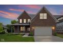 Beautiful two-story brick home with a covered front porch, an attached two-car garage, and well-manicured lawn at sunset at 6553 Stone Pointe Way, Indianapolis, IN 46237
