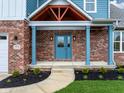 Inviting entryway with a blue front door, brick columns, and decorative landscaping at 7604 Brownstone Ct, Greenfield, IN 46140