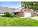 Inviting brick home with a two-car garage and a professionally landscaped lawn featuring mature shrubs and green grass at 1605 Leisure Way, Greenfield, IN 46140
