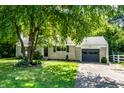 Single story home featuring a manicured lawn, gray garage, concrete driveway, and a tree in the front yard at 6491 N Oxford St, Indianapolis, IN 46220
