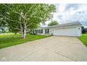 A white home with an attached two car garage and long driveway sits underneath a large tree canopy at 124 Bess Blvd, Pendleton, IN 46064