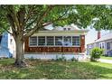 A charming brick home boasts a brick and white porch, complemented by a lush green lawn and mature trees at 1411 N Linwood Ave, Indianapolis, IN 46201