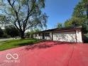 Inviting home with a red driveway, a two-car garage, and a lush green lawn with mature trees at 4014 Arquette Dr, Indianapolis, IN 46235