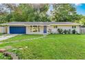 Charming single-story home featuring a blue door and garage against a lush green lawn and mature trees at 7643 S Delaware St, Indianapolis, IN 46227