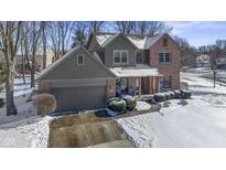 Two-story home showcasing its brick and siding exterior, complemented by a snow-covered yard and mature trees at 9955 Woodstock Way, Fishers, IN 46037