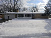 Brick ranch home with snow-covered yard, attached garage, and sunroom at 515 Wedgewood Dr, Anderson, IN 46013