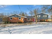 Brick and gray sided home with a red front door and snowy yard at 8810 W Tulip Tree Dr, Muncie, IN 47304