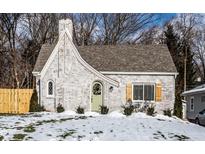 Charming white brick cottage with a green door, landscaping, and snow-covered lawn at 132 W 41St St, Indianapolis, IN 46208