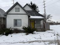 Charming white house with gray accents, yellow door, and snowy yard at 243 E Caven St, Indianapolis, IN 46225