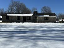 Ranch home with stone exterior, snow-covered yard, and mature trees at 7812 S 400 W, Columbus, IN 47201