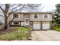 Split-level home with tan siding, white trim, attached two-car garage, and charming front yard at 9229 Thrushwood Ln, Indianapolis, IN 46250