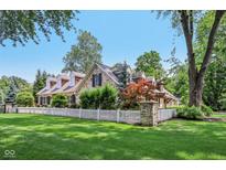 Charming stone home with a well-manicured lawn and white picket fence in a lush, green neighborhood at 7837 Dean Rd, Indianapolis, IN 46240