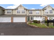 Two-story townhome featuring an attached garage, brick accents, and lush landscaping at 2231 Colfax Ln, Indianapolis, IN 46260