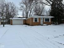 Charming single-story brick home with attached garage surrounded by snow-covered yard and bare trees at 10229 Baribeau Ln, Indianapolis, IN 46229