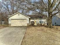 Cozy single-story home featuring a yellow front door, attached garage, and mature trees at 5430 Milhouse Rd, Indianapolis, IN 46221