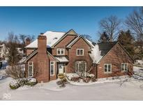 Charming red brick two-story home with white trim and snow-covered roof, set in a landscaped yard at 12978 Portsmouth Dr, Carmel, IN 46032