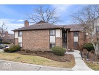 Brick condo building features neutral trim, a chimney, well-maintained landscaping, and sidewalk entrance at 2235 Rome Dr # D, Indianapolis, IN 46228