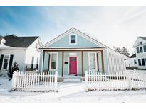 Charming home featuring a covered porch, pink front door, and white picket fence, all surrounded by a blanket of fresh snow at 205 S Market St, Thorntown, IN 46071