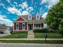 Charming two-story home featuring red siding, black shutters,dormer windows, front porch and a well-manicured lawn at 12964 Walbeck Dr, Fishers, IN 46037