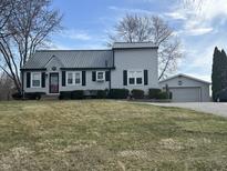 Charming one-story home features gray siding, black shutters and a metal roof with a detached garage in the background at 1905 Apple St, Greenfield, IN 46140