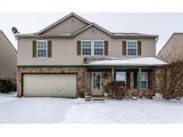 Two-story home featuring a two-car garage and charming front porch, covered in winter snow at 10991 Clear Spring Dr, Camby, IN 46113