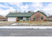 Charming brick home featuring a green roof, covered porch, attached garage, and tidy landscaping at 1586 Woodside Dr, Danville, IN 46122