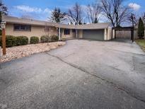 Wide shot of ranch-style home with attached garage and carport with paved driveway and mature landscaping at 2933 E 62Nd St, Indianapolis, IN 46220
