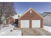 Charming red brick home featuring an attached two car garage and snow covered front yard at 7664 Waterwood Dr, Indianapolis, IN 46214