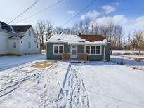 Charming exterior view of a light green single story home with a brown roof and snowy yard at 1235 Indiana Ave, Anderson, IN 46012