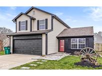 Charming two-story home featuring a gray garage door, red front door, sidewalk, and wagon wheel accent at 1013 Redwood Dr, Lebanon, IN 46052