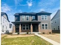 Two-story home with gray siding, brick accents, covered porch, and neat landscaping at 14390 Bishop Birch Pl, Carmel, IN 46032